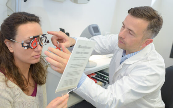 Female patient wearing opticians testing glasses supported by a male Optometrist By auremar
